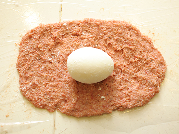 ラップの上に薄く肉ダネを広げ、中央にゆで卵をおく