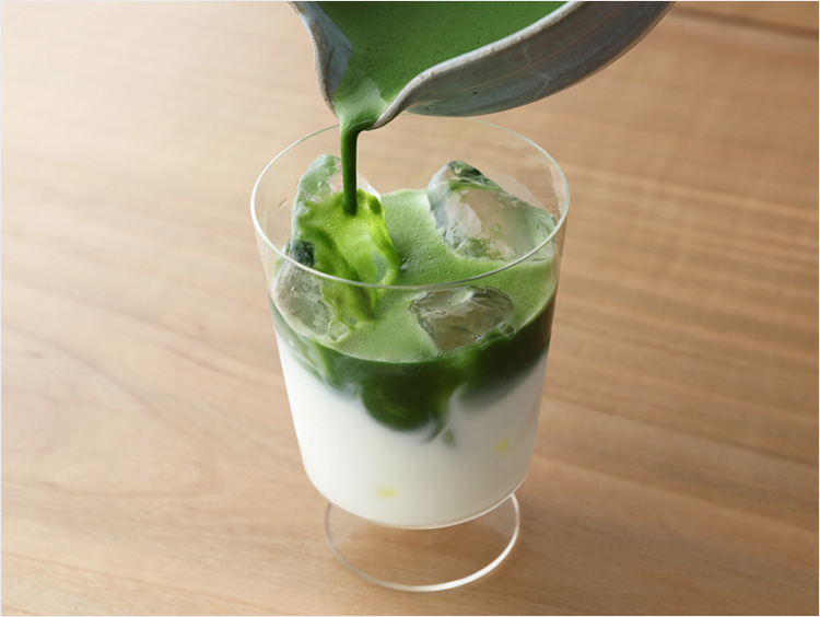 牛乳と氷が入ったグラスに抹茶を注ぎ、アイス抹茶ラテを作る様子